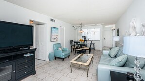 A modern living room with a flat-screen TV, a sofa, a coffee table, and a dining area with chairs and a table. - Discover the Epitome of Waterfront Living in this Stunning condo on Isla del Sol!~ (St Petersburg)