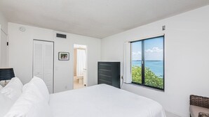 A bedroom with a large bed, a wardrobe, a desk, and a window with a view of the sea. - Discover the Epitome of Waterfront Living in this Stunning condo on Isla del Sol!~ (St Petersburg)