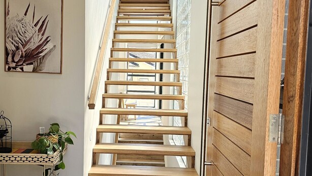 A wooden staircase leading to a second floor, with a view of the sky through a window at the top.