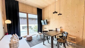 A cozy room with a sofa, a dining table with chairs, a TV mounted on the wall, and a view of the outside balcony.