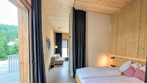 A modern hotel room with a wooden ceiling, a large bed with white bedding, a sofa, and a view of a forested area.