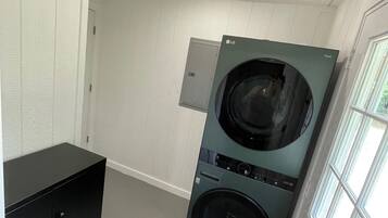 A laundry room with a front-loading washer and dryer, a black storage cabinet, and a window providing natural light.