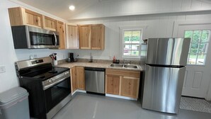 A modern kitchen with wooden cabinets, stainless steel appliances, and a window providing natural light. - Nate’s Place (Sallisaw)