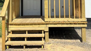 A wooden deck with a white door and a window, number 812 on the post, and a small porch area. - Nate’s Place (Sallisaw)