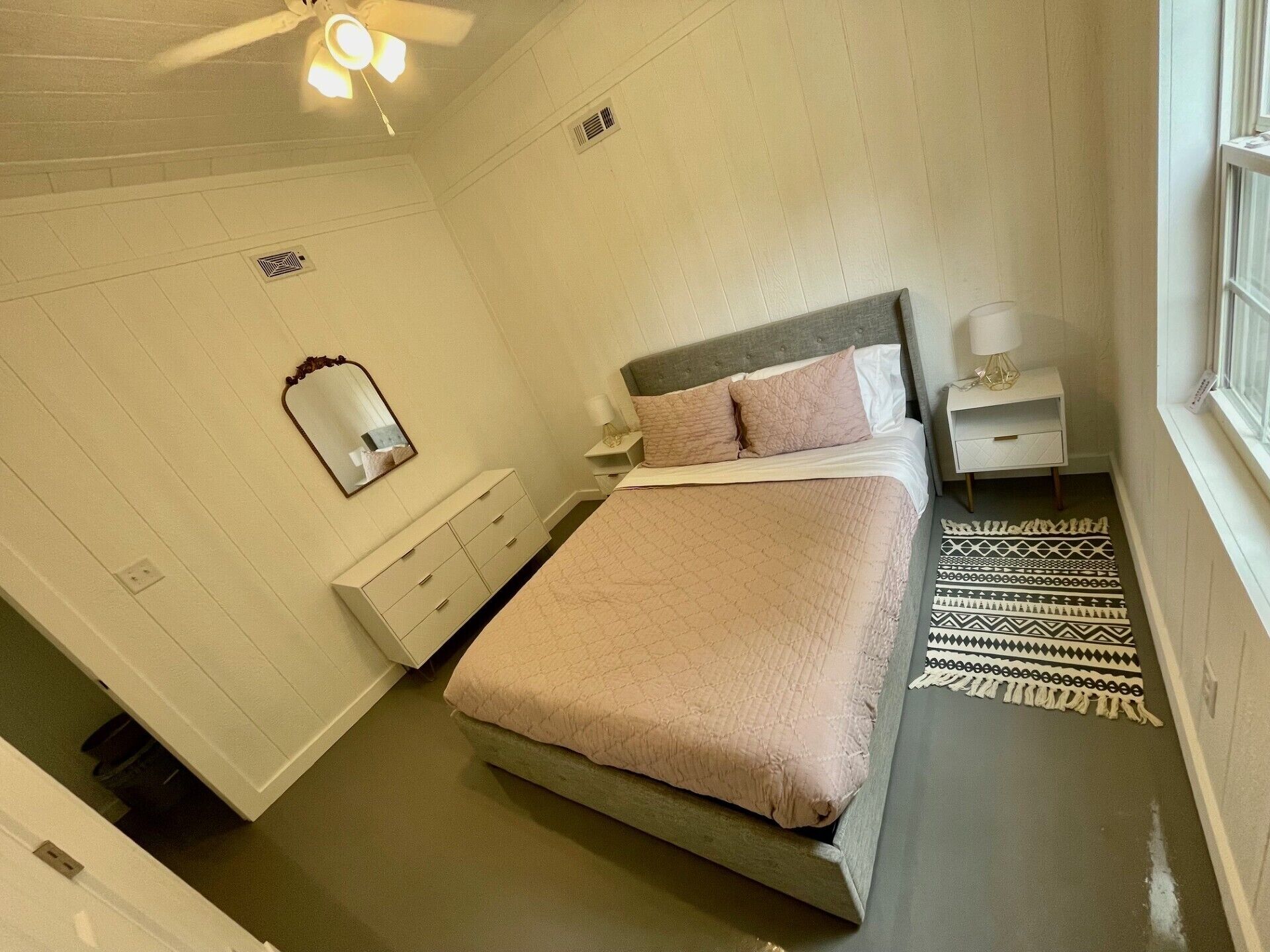 A bedroom with a bed, a nightstand, a dresser, a mirror, and a ceiling fan.