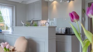 Cozinha com armários brancos, um lustre e uma sala de jantar com uma mesa posta com maçãs verdes e tulipas.
