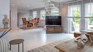 A spacious living area with a dining table, chairs, a TV, and a staircase. - Rosen/horstweg 5 - Ferienhaus "rosen/horstweg 5" in Alt-westerland/tinnum (Sylt)