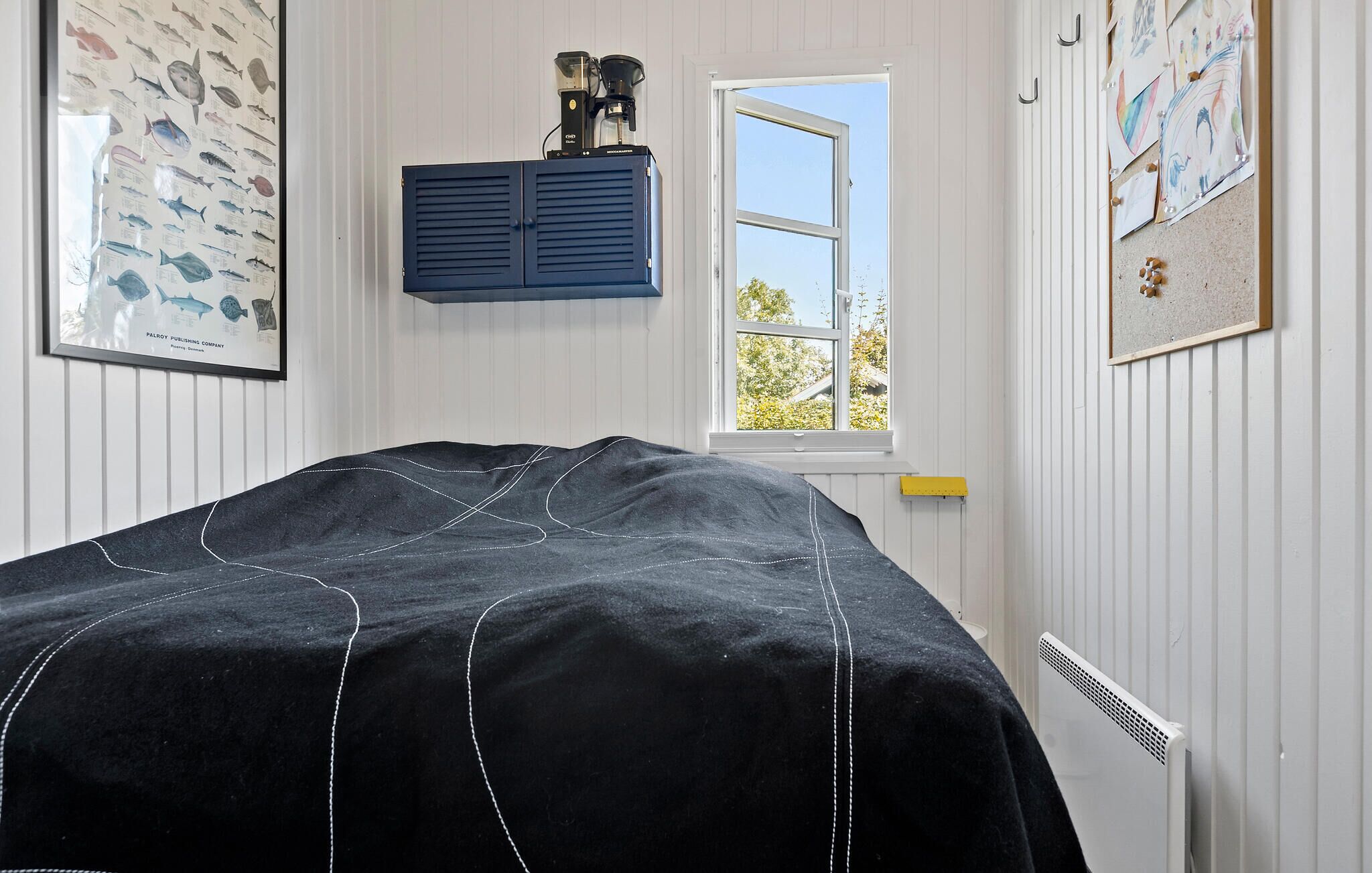 Un dormitorio con cama, ventana, radiador y adornos en la pared, incluyendo una tabla de peces y un cuadro enmarcado.