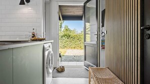 Cucina compatta con lavatrice, un piccolo bancone e una porta che dà su un’area esterna con vista sul verde.