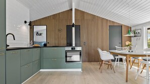 Una cucina moderna con mobili verdi, forno integrato e zona pranzo con sedie bianche e tavolo in legno.