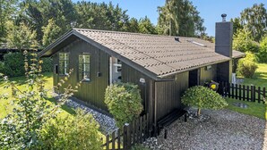 Una piccola casa di legno scuro con tetto spiovente, un camino e un vialetto sterrato.