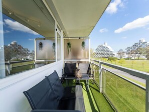Ein Balkon mit Blick auf moderne Gebäude, einer Glasbrüstung und einer Sitzecke mit Tisch und Stühlen.