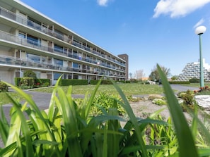 A multi-story hotel with balconies, a parking area, and a well-maintained garden.