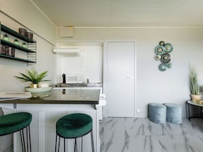 A modern kitchen with a white door, a microwave, and a stove. There are green stools and a small table with decorative plates.