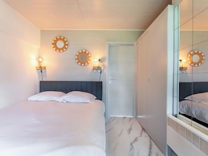 A bedroom with a bed, two wall-mounted light fixtures, a door, and a mirrored wardrobe.