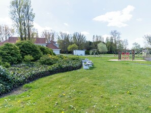 A grassy outdoor area with a picnic table, a swing set, and a small shed.