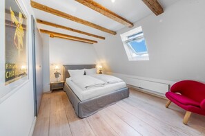 Ein Schlafzimmer mit einem Bett, Holzbalken, einem Oberlicht, einem roten Sessel und einem Poster an der Wand.