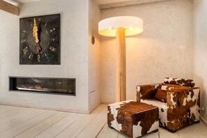 Een moderne woonkamer met een open haard, een groot abstract schilderij, een houten vloer en een bank met koeienhuidpatroon.
