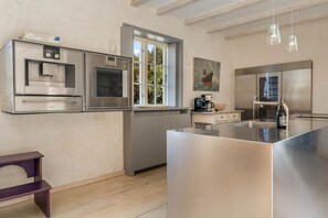 Une cuisine moderne dotée d’appareils électroménagers en acier inoxydable, d’une grande fenêtre et de luminaires suspendus.