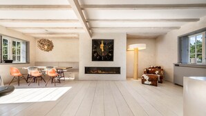 Een ruime woonkamer met een open haard, een eethoek met oranje stoelen en een groot raam.