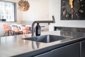 Een moderne keuken met een roestvrijstalen spoelbak, een zeepdispenser en een klok aan de muur.