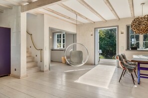 Ein modernes Interieur mit einem Hängekorbstuhl, einem Essbereich und einer Treppe, die zu einem Außenbereich führt.