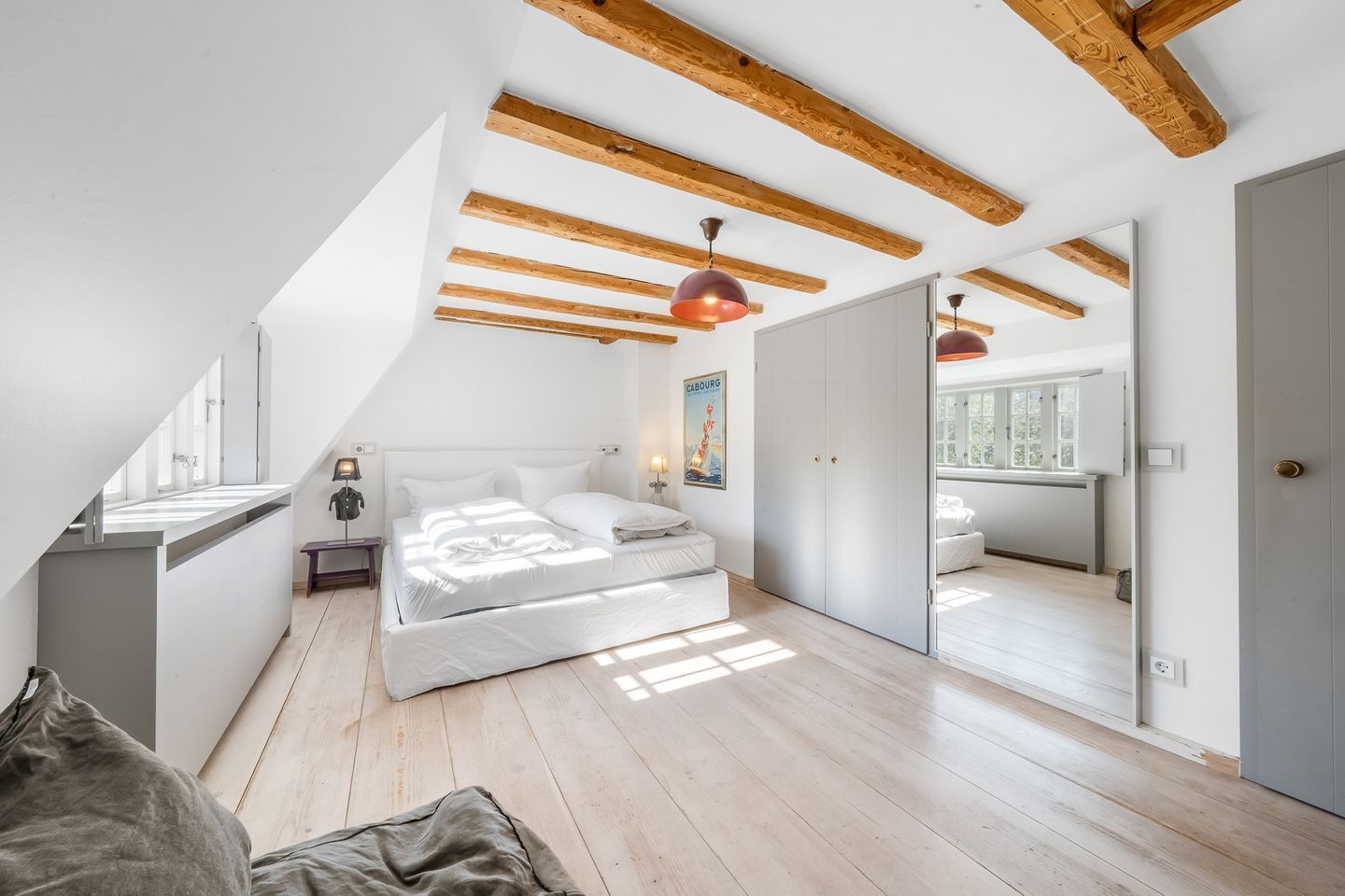 Un dormitorio con techo estilo loft, vigas de madera, una cama con ropa blanca, una mesita de noche, una lámpara y un cartel en la pared.