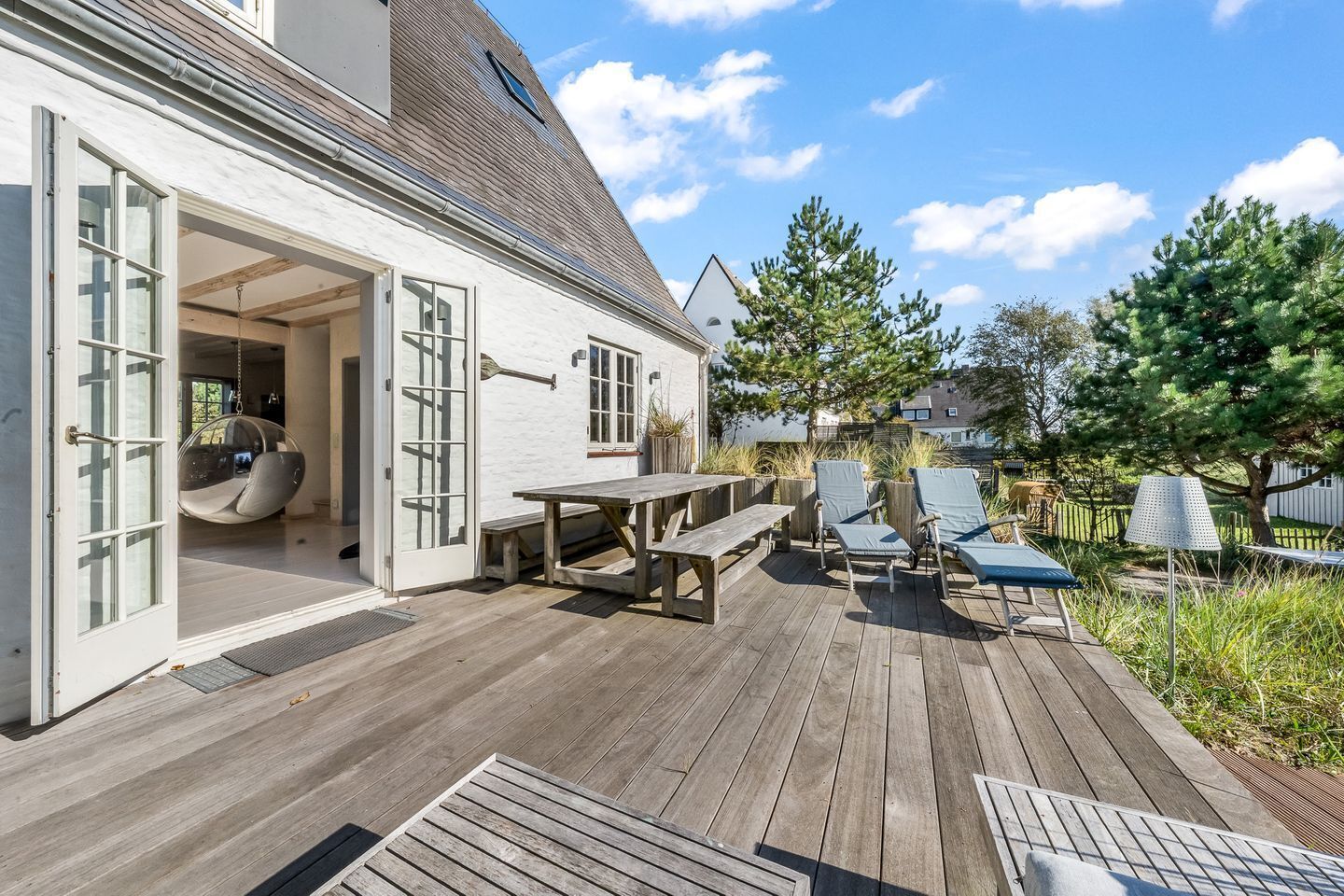 Une terrasse en bois avec une table et des chaises, un fauteuil suspendu et une pergola.