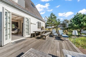 Een houten terras met een tafel, stoelen, een hangstoel en een pergola.