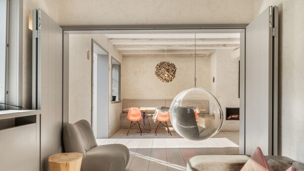 Een moderne woonkamer met een grote hangstoel in bolvorm van glas, een open haard en een eethoek met oranje stoelen.
