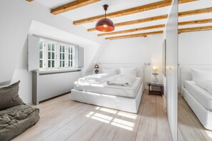 A bedroom with a sloped ceiling, a bed with white bedding, a bedside table with a lamp, and a window with white shutters.