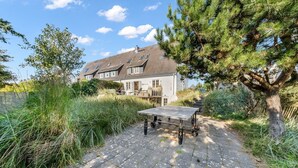 Een huis met een verhard terras, een tafel op wielen en een grote boom.