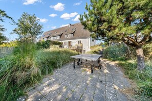 A house with a paved patio, a table with wheels, and a large tree. - Lighthouse 2 - Exklusiv. Modern. Hochwertig. Strandnah (Hörnum (Sylt))