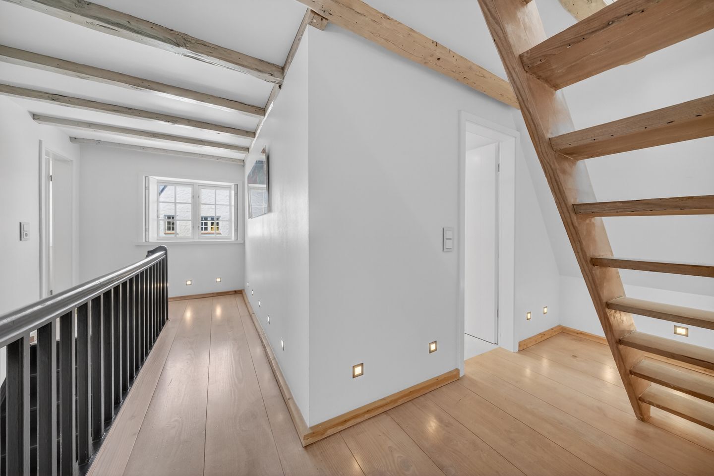 Un intérieur avec un escalier en bois, des murs blancs et un plancher en bois.