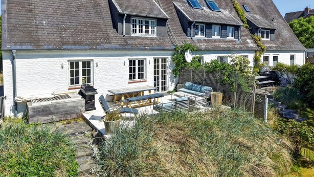 A two-story house with a white exterior, a patio with outdoor furniture, and a garden area. - Lighthouse 4 - Exklusiv. Modern. Hochwertig. Strandnah (Hörnum (Sylt))