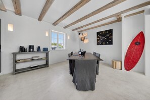 A modern kitchen with a dining area, a large window, and a surfboard on the wall.