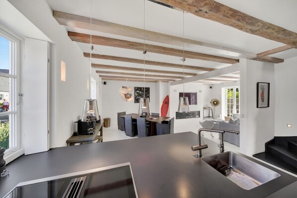A modern kitchen with a central island, pendant lighting, and exposed wooden beams.