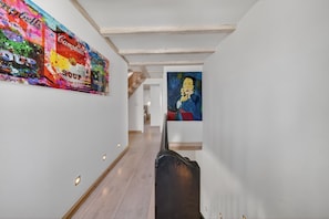 Un couloir aux murs blancs, orné de poutres en bois et de tableaux.