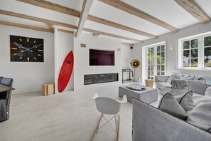 A modern living room with a fireplace, a surfboard, and a dining area.