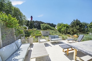 Eine Terrasse im Freien mit einer Couch, zwei Liegestühlen, einem Tisch und einem kleinen Schuppen.