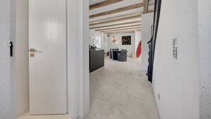 A hallway with a white door, a kitchen area with a dining table, and exposed wooden beams on the ceiling. - Lighthouse 4 - Exklusiv. Modern. Hochwertig. Strandnah (Hörnum (Sylt))