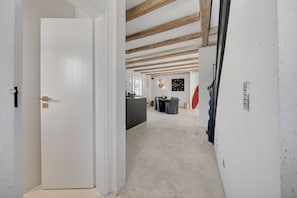A hallway with a white door, a kitchen area with a dining table, and exposed wooden beams on the ceiling. - Lighthouse 4 - Exklusiv. Modern. Hochwertig. Strandnah (Hörnum (Sylt))