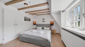 A bedroom with a bed, wooden beams, a window, and wall-mounted lights. - Lighthouse 4 - Exklusiv. Modern. Hochwertig. Strandnah (Hörnum (Sylt))