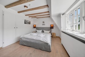 A bedroom with a bed, wooden beams, a window, and wall-mounted lights. - Lighthouse 4 - Exklusiv. Modern. Hochwertig. Strandnah (Hörnum (Sylt))