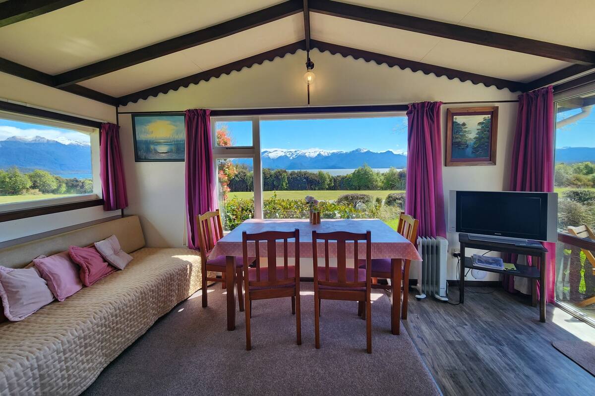 Una habitación acogedora con una mesa de comedor, sillas, un sofá y un televisor. Cuenta con ventanas amplias y vistas a la montaña.