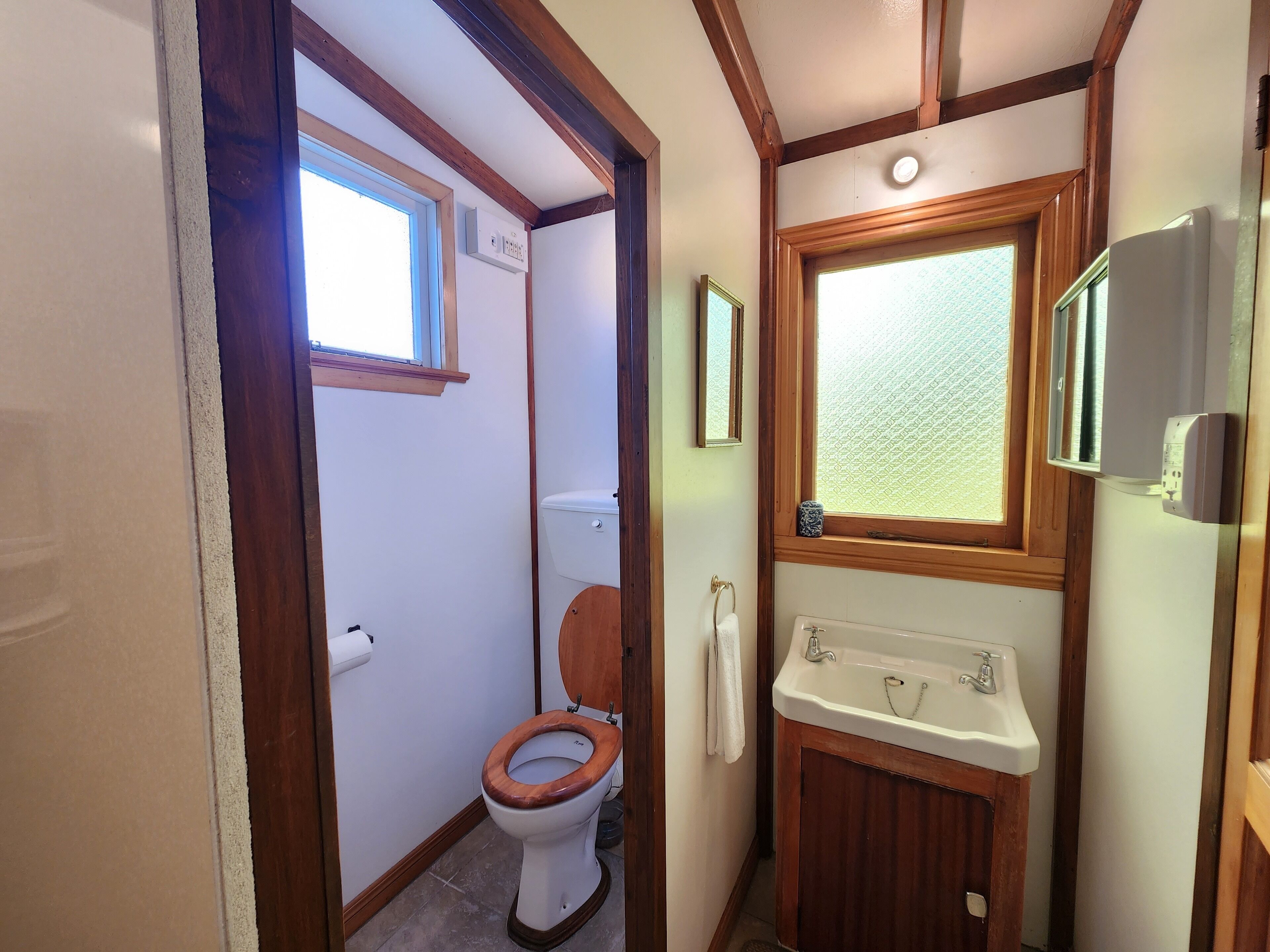 A compact bathroom with a wooden toilet, a sink, and a window providing natural light.