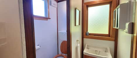A compact bathroom with a wooden toilet, a sink, and a window providing natural light.