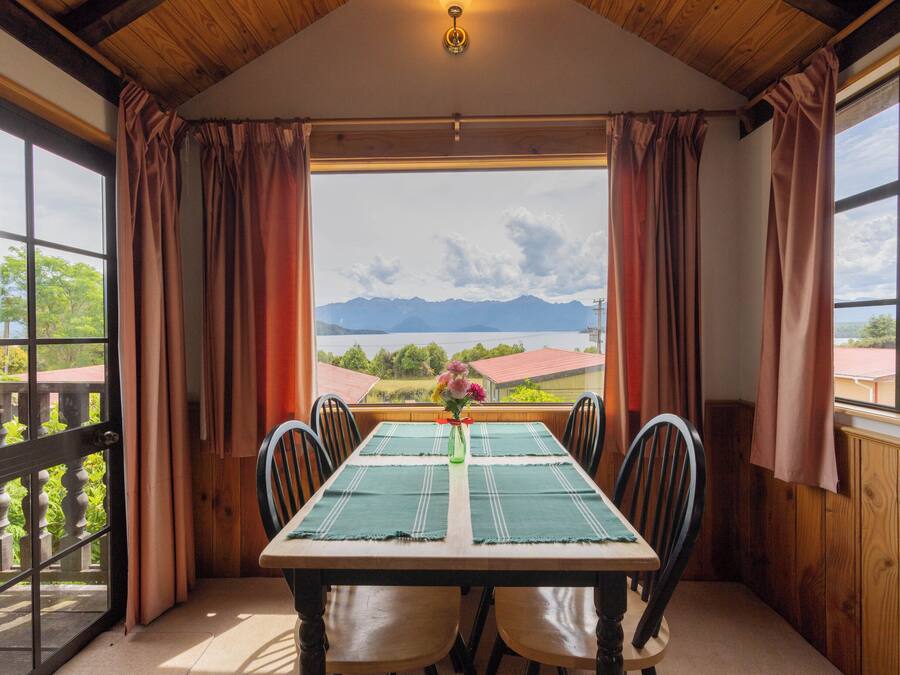A dining area with a table set for four, large windows with curtains, and a view of mountains and greenery.