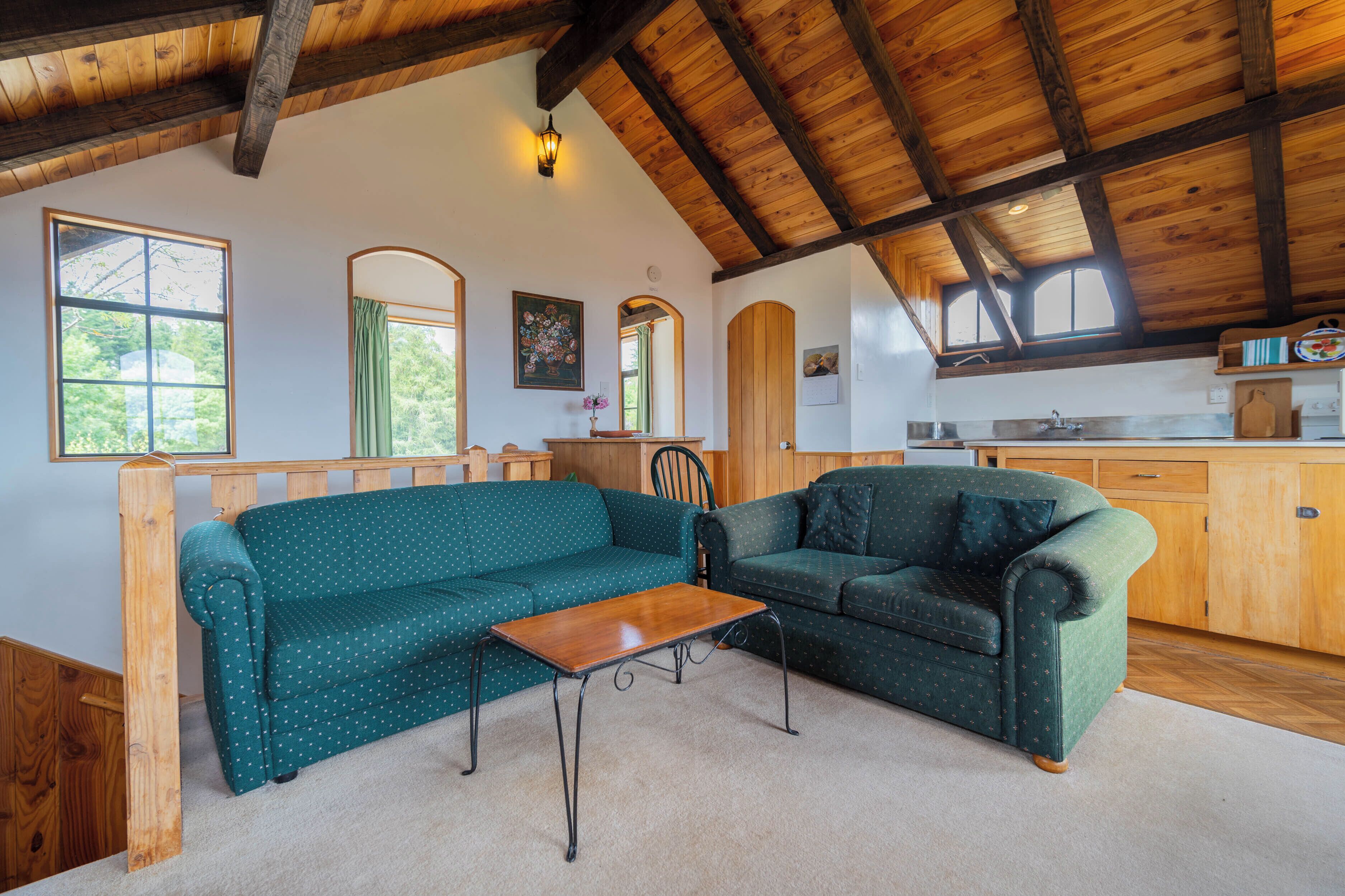 Una sala de estar acogedora con dos sofás verdes, una mesa de centro de madera y techo de madera.