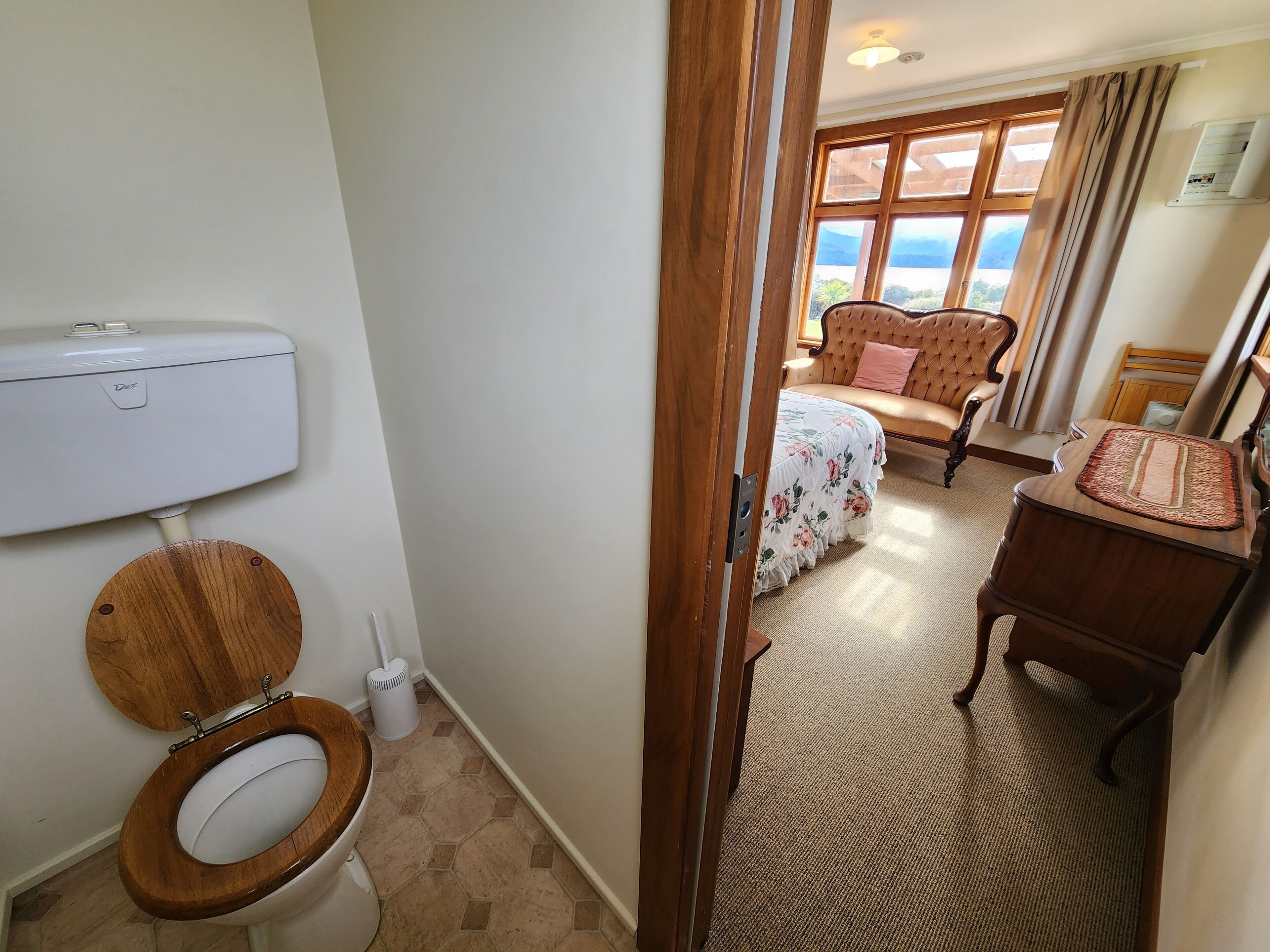 A bathroom with a wooden toilet, a white toilet paper holder, and a white trash bin.